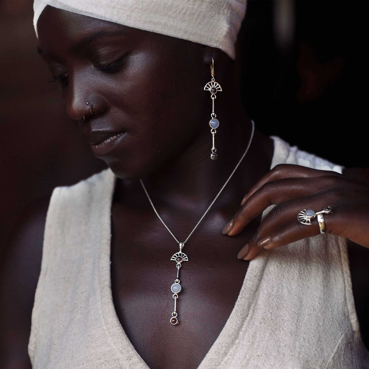 A woman wearing a white headscarf and sleeveless top showcases a matching set of sterling silver 925 jewelry, including earrings, a necklace, and a ring. Each piece features decorative silver elements and rhinestone crystal with round stones, centered around the Peace of Mind Pendant from Kaora Sandara Jewelry.