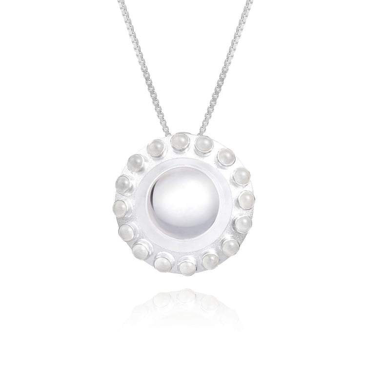 The Silver Pendant Energy Transformer with Crystal from Kaora Sandara Jewelry features a circular design, showcasing a smooth white center adorned with a decorative border of small pearl-like beads and shimmering rhinestone crystals, all elegantly suspended on a delicate chain.