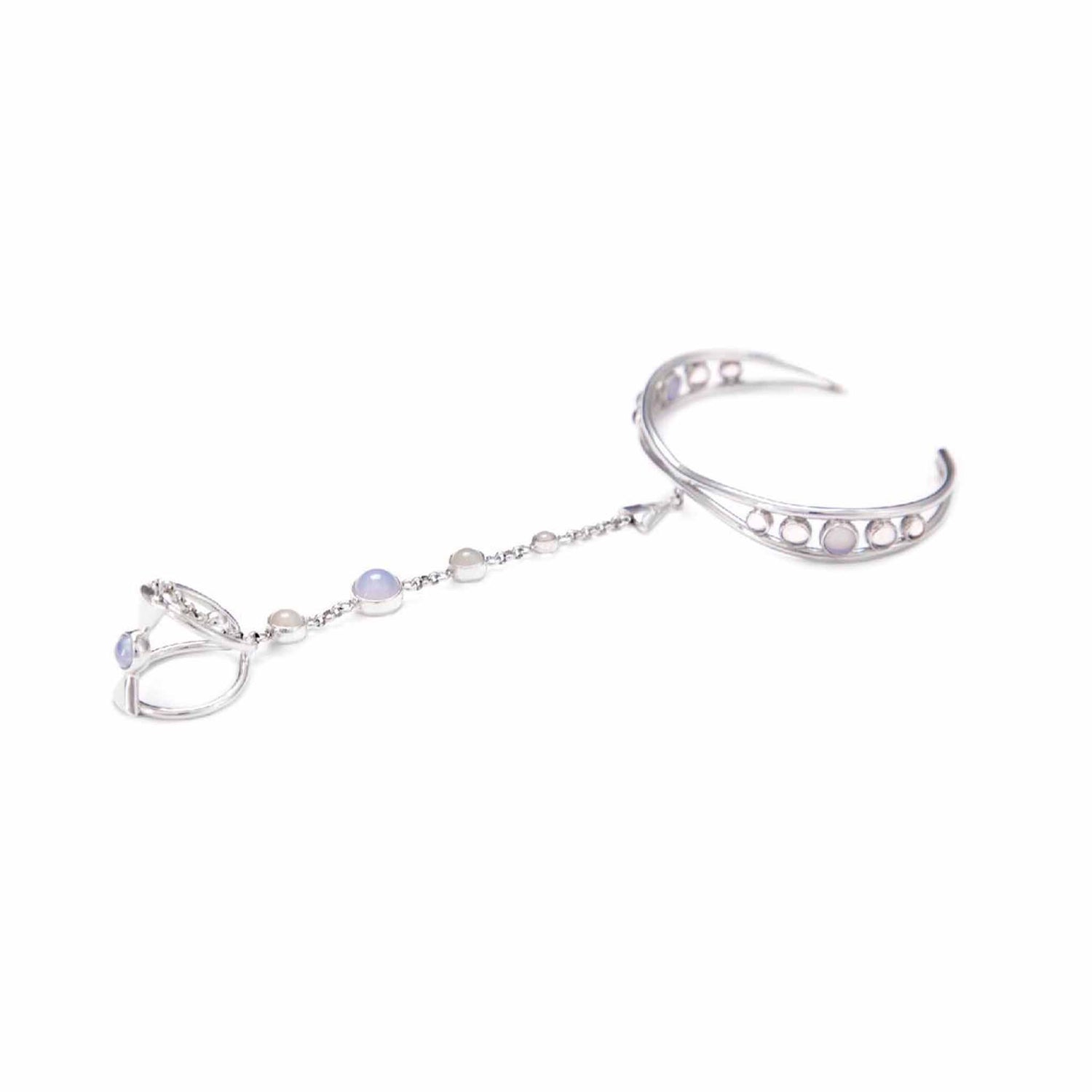 The Kaora Sandara Jewelry Silver Hand Chain Goddess Path is an elegant sterling silver 925 adjustable bracelet connected to a ring by a delicate chain. It is adorned with small Chalcedony and Crystal Sphere gemstones. The bracelet features an open crescent moon design with circular cutouts, giving it an intricate and sophisticated look, perfect for the Divine Woman.