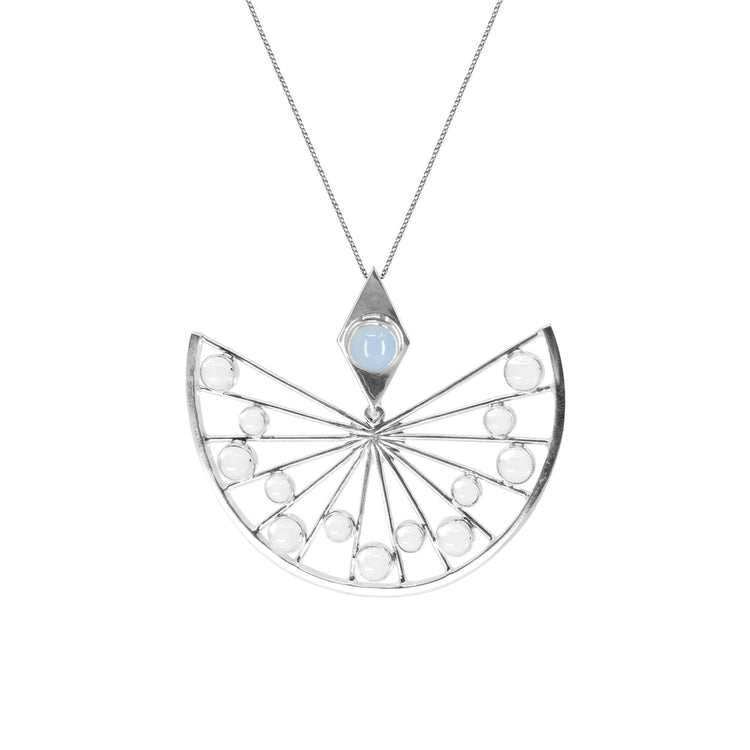 The Higher Self Pendant in sterling silver from Kaora Sandara Jewelry showcases an intricate, fan-like design. This semi-circular pendant features spokes radiating from the center, adorned with small round crystals. A single larger chalcedony gemstone is set within a diamond-shaped frame above the fan, enhancing its spiritual allure.