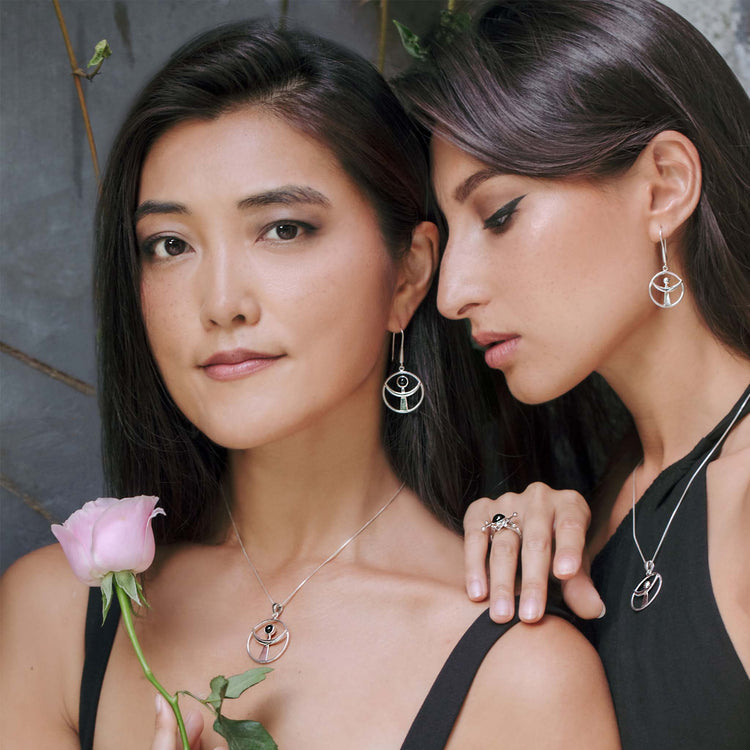 Two women with long dark hair are showcasing elegant Sterling Silver 925 jewelry from Kaora Sandara Jewelry. The woman on the left holds a pink rose and wears a necklace with a circular pendant. The woman on the right, leaning towards the left, wears matching Releasing From the Deepest Fears Earhooks in Sterling Silver, size S, and a ring, gently resting her hand on the other's shoulder.